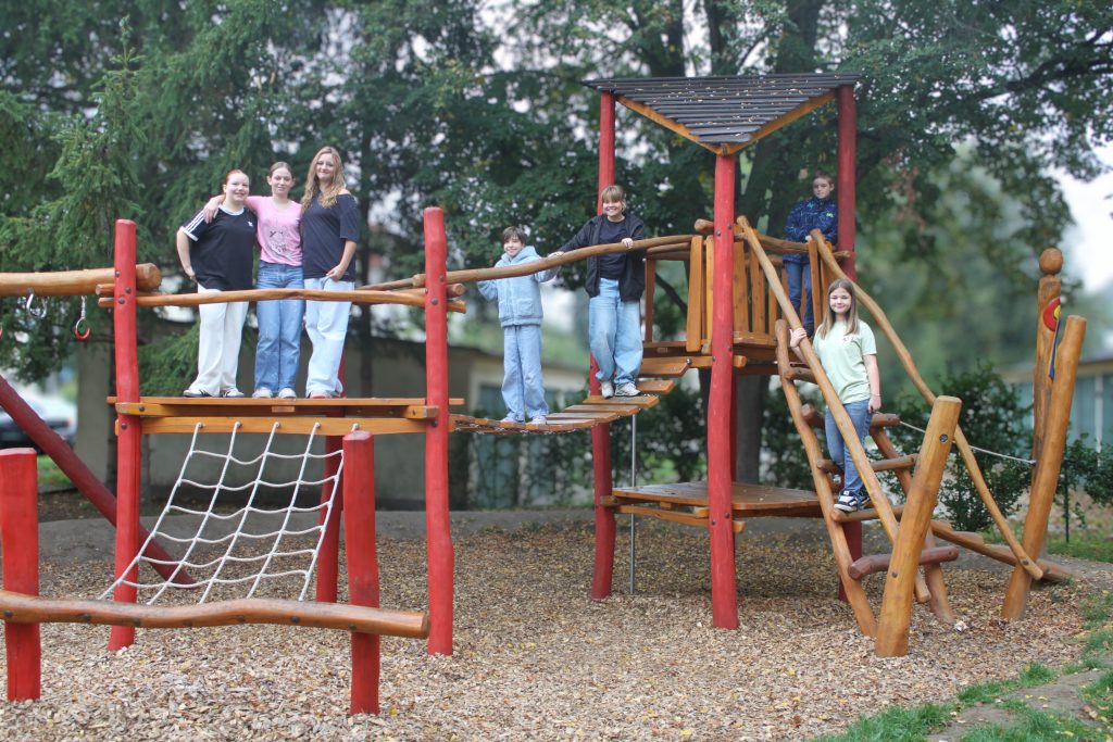 Sechs Kinder und Jugendliche stehen auf und um ein Klettergerüst aus Holz herum.